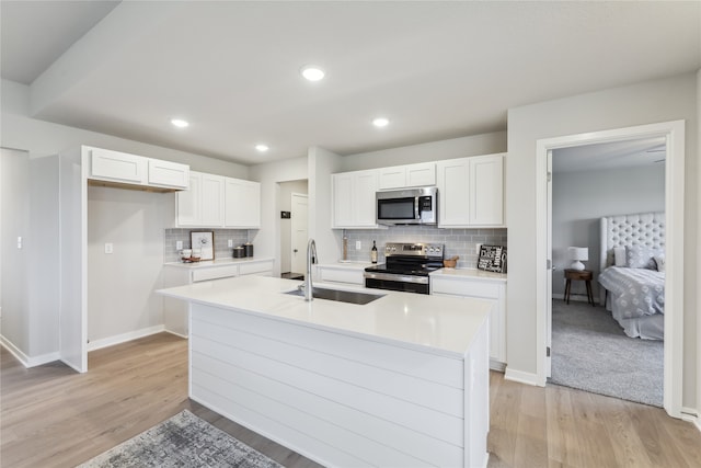 kitchen with white cabinets, appliances with stainless steel finishes, light hardwood / wood-style floors, and an island with sink