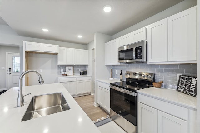 kitchen featuring appliances with stainless steel finishes, backsplash, sink, white cabinets, and light hardwood / wood-style floors