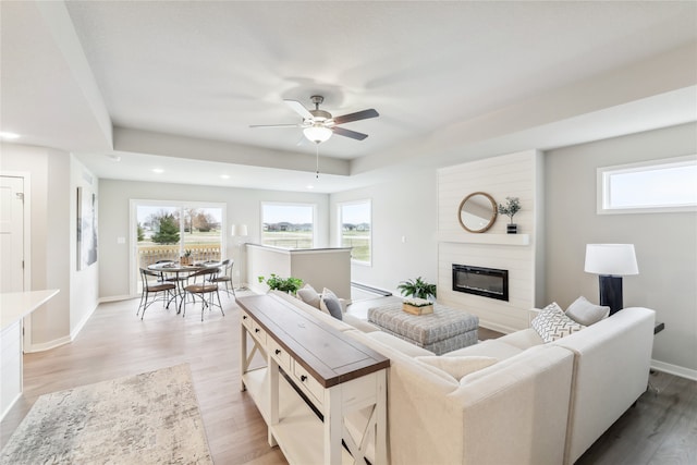 living room with a fireplace, light wood-type flooring, and ceiling fan