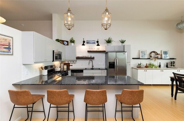 kitchen with tasteful backsplash, stainless steel appliances, sink, kitchen peninsula, and light wood-type flooring