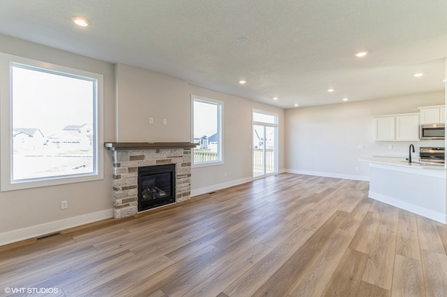 unfurnished living room featuring sink, light hardwood / wood-style flooring, a stone fireplace, and a textured ceiling