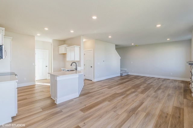 kitchen featuring white cabinetry, sink, light wood-type flooring, and a center island with sink