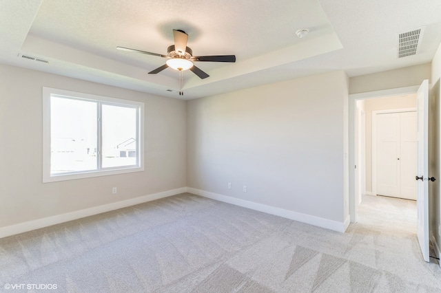 unfurnished room with a textured ceiling, ceiling fan, light colored carpet, and a raised ceiling