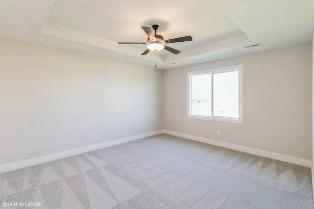 empty room with ceiling fan, a raised ceiling, and carpet floors