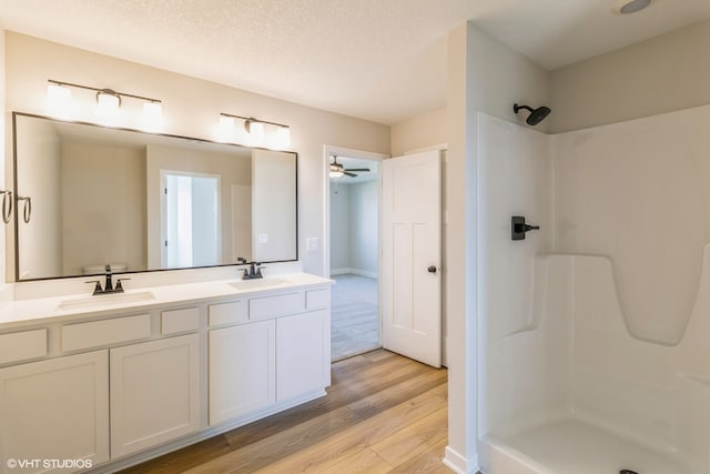 bathroom with ceiling fan, a textured ceiling, wood-type flooring, a shower, and vanity