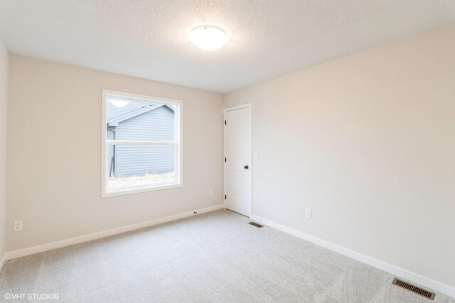 unfurnished room featuring light carpet, baseboards, visible vents, and a textured ceiling