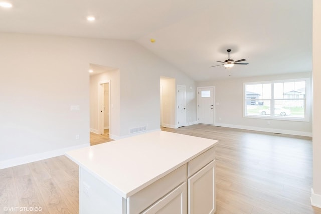 kitchen featuring light wood-style flooring, visible vents, a ceiling fan, vaulted ceiling, and a center island