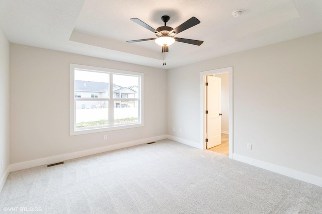 carpeted empty room featuring a tray ceiling, visible vents, ceiling fan, and baseboards