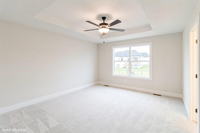 empty room with baseboards, a tray ceiling, a textured ceiling, and light colored carpet