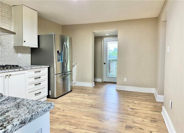 kitchen featuring light wood-type flooring, white cabinets, stainless steel appliances, light stone countertops, and wall chimney range hood