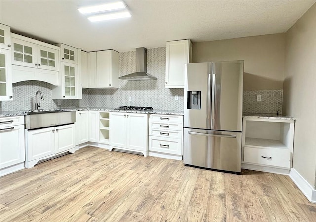 kitchen featuring wall chimney range hood, appliances with stainless steel finishes, light stone counters, light hardwood / wood-style floors, and white cabinets