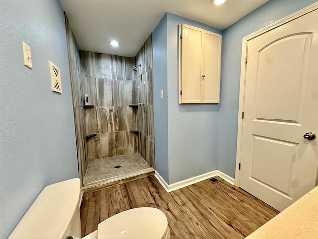 bathroom featuring wood-type flooring, toilet, and tiled shower