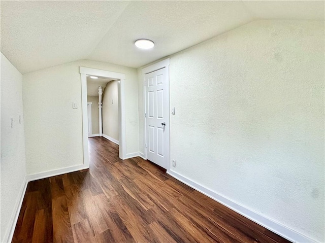 unfurnished room featuring lofted ceiling, dark hardwood / wood-style flooring, and a textured ceiling