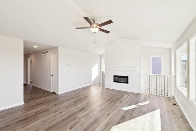 unfurnished living room with hardwood / wood-style flooring, vaulted ceiling, a large fireplace, and ceiling fan