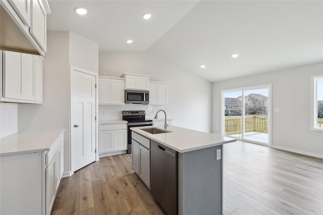 kitchen with appliances with stainless steel finishes, vaulted ceiling, sink, a center island with sink, and white cabinets