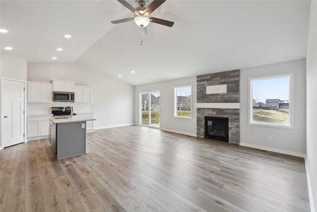 interior space featuring a fireplace, stainless steel appliances, white cabinets, lofted ceiling, and an island with sink