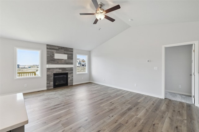 unfurnished living room featuring ceiling fan, a large fireplace, vaulted ceiling, and light hardwood / wood-style flooring