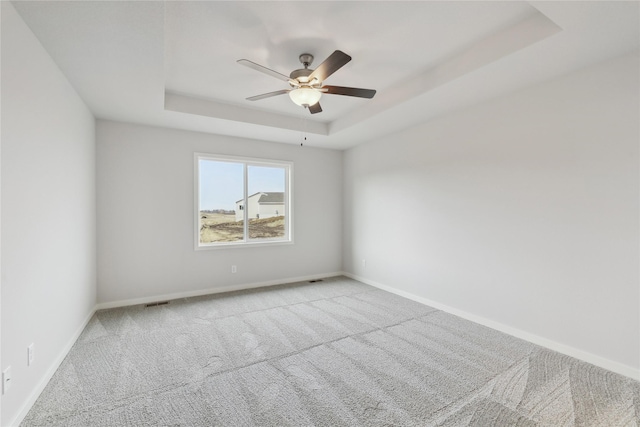 carpeted empty room featuring ceiling fan and a raised ceiling