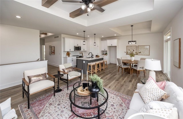 living room with ceiling fan, light hardwood / wood-style floors, sink, and a tray ceiling