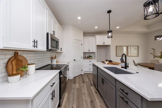 kitchen with white cabinetry, stainless steel appliances, hanging light fixtures, sink, and light hardwood / wood-style floors