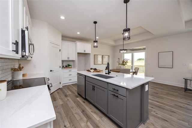 kitchen with white cabinetry, a tray ceiling, decorative backsplash, sink, and light hardwood / wood-style flooring