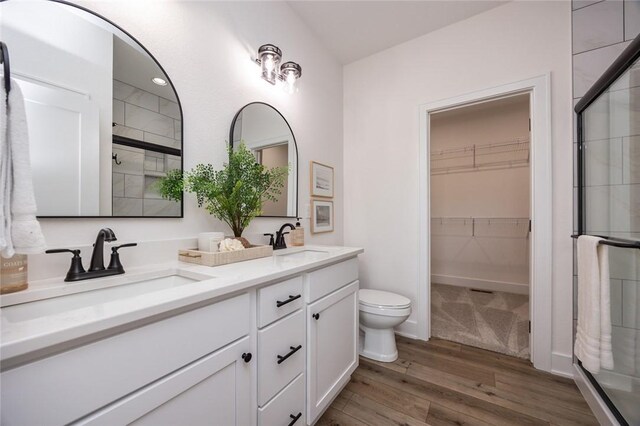 bathroom with walk in shower, hardwood / wood-style flooring, double sink vanity, and toilet