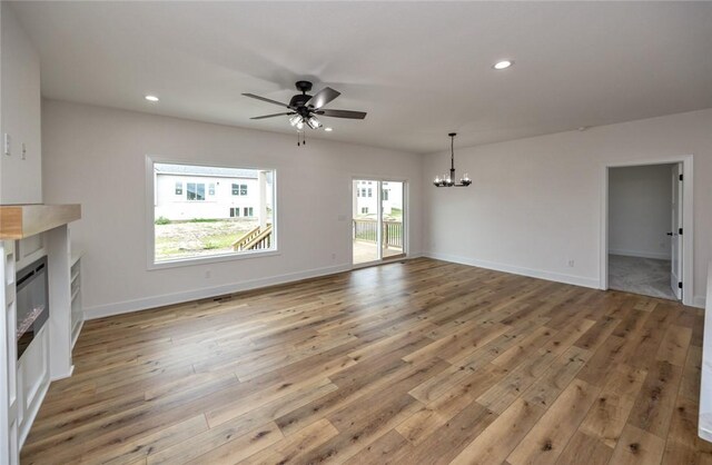 unfurnished living room with ceiling fan with notable chandelier and hardwood / wood-style floors