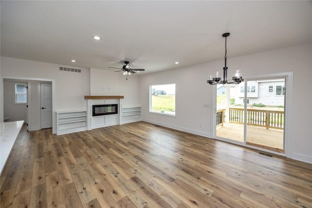 unfurnished living room with ceiling fan with notable chandelier and light hardwood / wood-style flooring