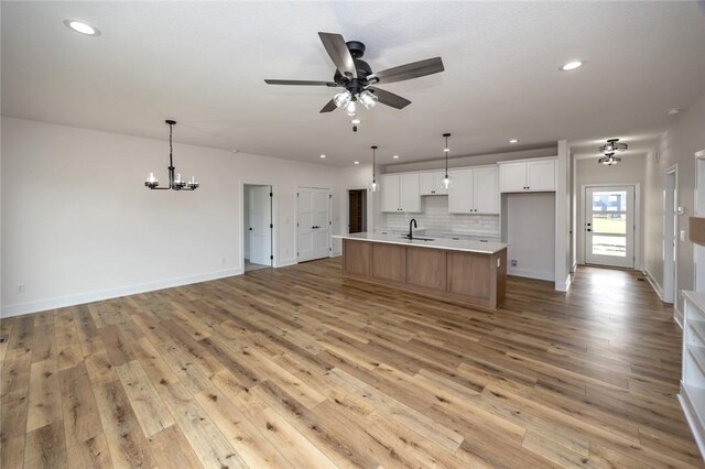 kitchen with white cabinets, sink, a center island with sink, light hardwood / wood-style flooring, and backsplash