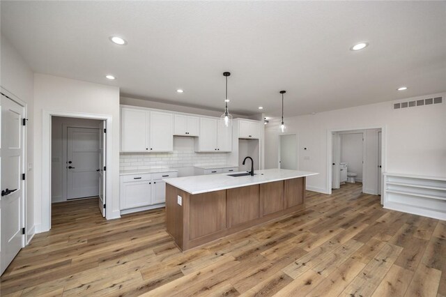 kitchen with light hardwood / wood-style flooring, white cabinets, an island with sink, decorative backsplash, and sink