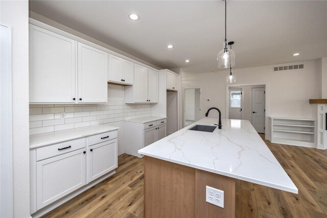 kitchen featuring sink, light hardwood / wood-style flooring, white cabinets, and a kitchen island with sink