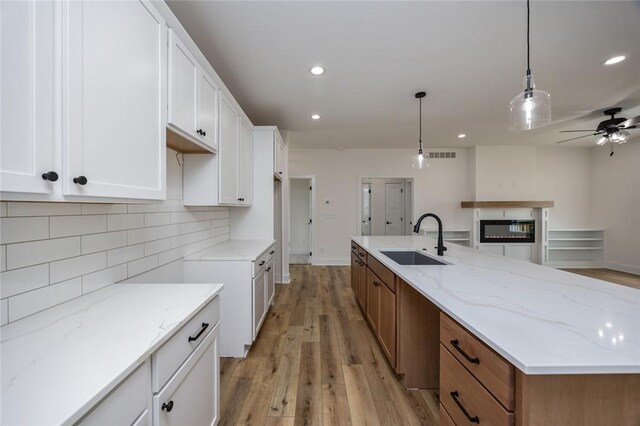 kitchen featuring white cabinetry, ceiling fan, light hardwood / wood-style floors, light stone countertops, and sink