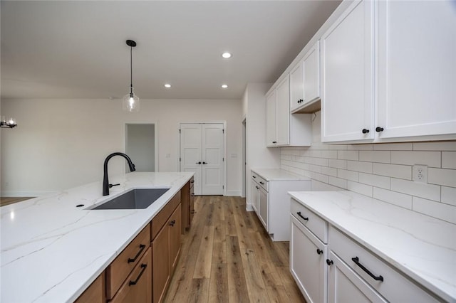 kitchen with white cabinets, light wood-type flooring, decorative light fixtures, and sink