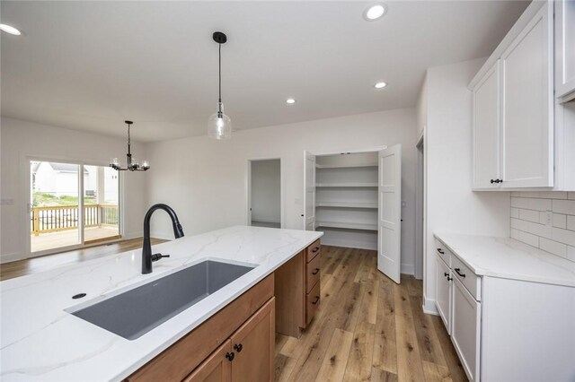 kitchen with sink, hanging light fixtures, light hardwood / wood-style floors, light stone countertops, and white cabinetry