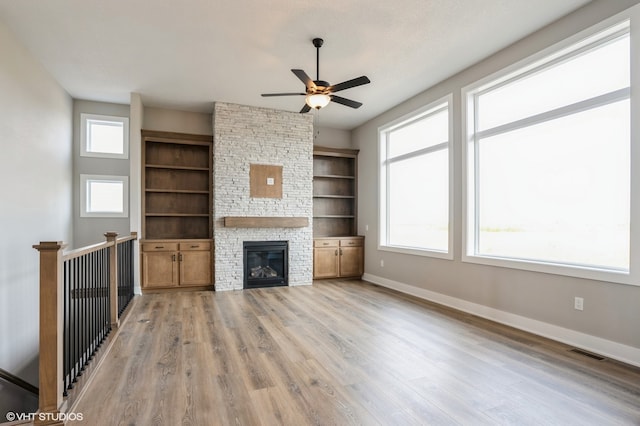 unfurnished living room with ceiling fan, a healthy amount of sunlight, light hardwood / wood-style flooring, and a fireplace