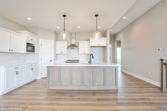 kitchen featuring white cabinets, wall chimney range hood, sink, and a kitchen island with sink