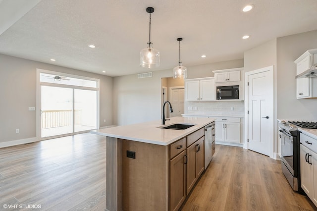 kitchen with appliances with stainless steel finishes, sink, light hardwood / wood-style floors, white cabinets, and a kitchen island with sink