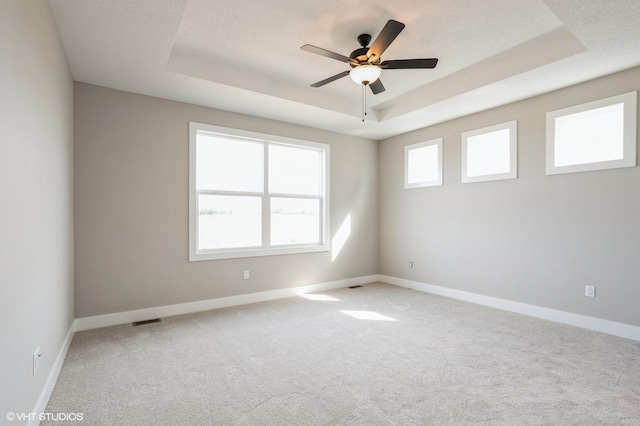 carpeted spare room with ceiling fan and a raised ceiling