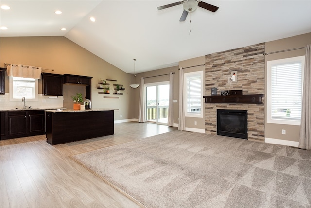 kitchen featuring dark brown cabinets, a large fireplace, a center island, light carpet, and ceiling fan