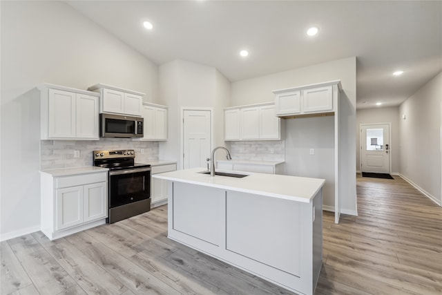 kitchen with sink, appliances with stainless steel finishes, an island with sink, white cabinets, and light wood-type flooring