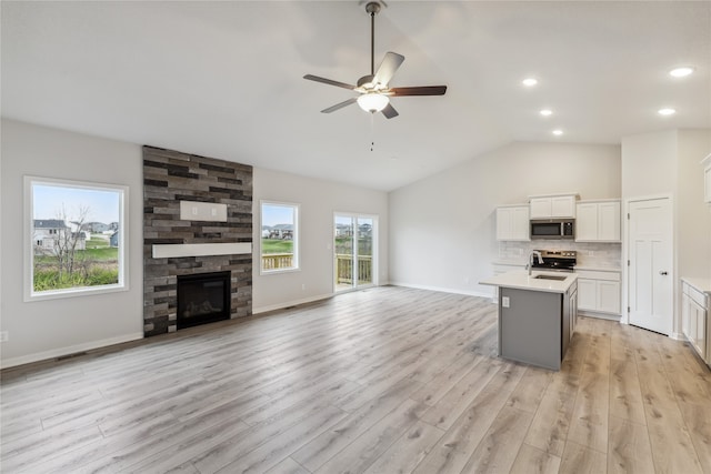 kitchen with light wood-type flooring, stainless steel appliances, vaulted ceiling, white cabinets, and an island with sink