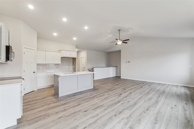 kitchen featuring lofted ceiling, ceiling fan, an island with sink, light hardwood / wood-style floors, and white cabinetry