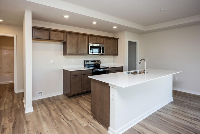 kitchen with sink, dark brown cabinets, light hardwood / wood-style flooring, an island with sink, and stainless steel appliances