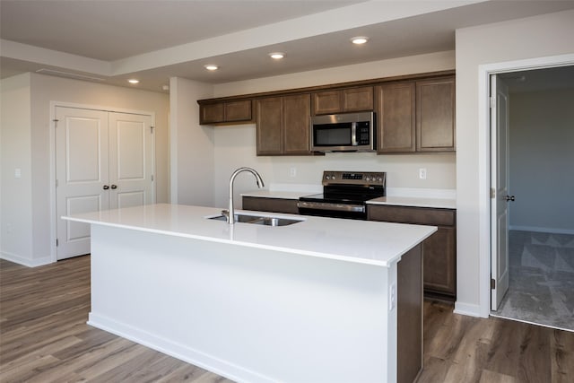 kitchen with sink, stainless steel appliances, dark brown cabinetry, a center island with sink, and light wood-type flooring