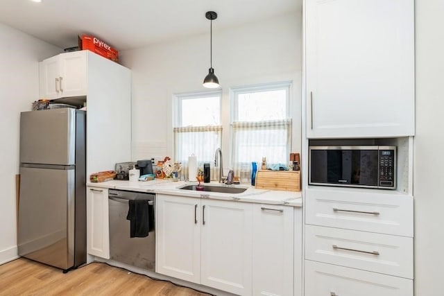 kitchen with appliances with stainless steel finishes, light hardwood / wood-style floors, white cabinetry, sink, and light stone counters