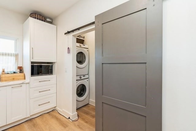 laundry area featuring light wood-type flooring, a barn door, and stacked washer and dryer