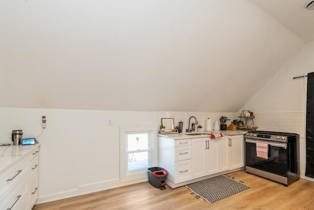 kitchen featuring sink, lofted ceiling, light hardwood / wood-style floors, stainless steel range, and white cabinets