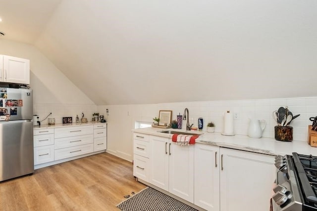 kitchen with light hardwood / wood-style flooring, white cabinetry, sink, stainless steel fridge, and vaulted ceiling