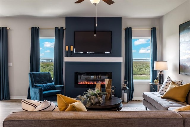 living room featuring ceiling fan, a large fireplace, and light hardwood / wood-style floors