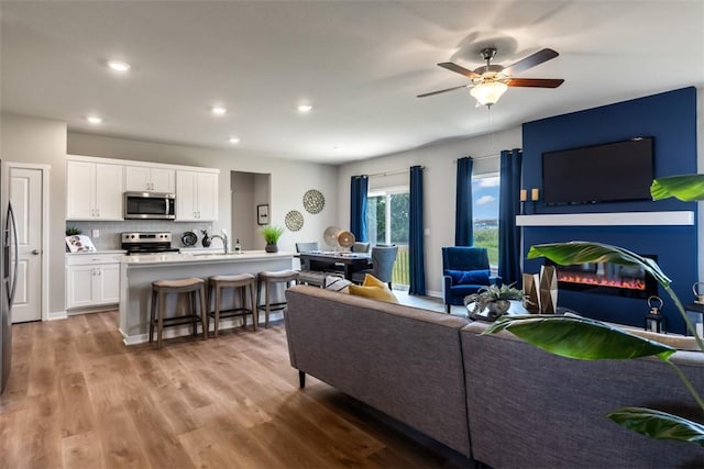 living room featuring ceiling fan, sink, and light wood-type flooring